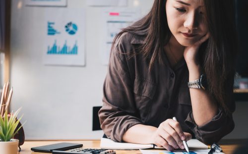 woman sitting with her hand on her chin doing paperwork figuring out financial matters